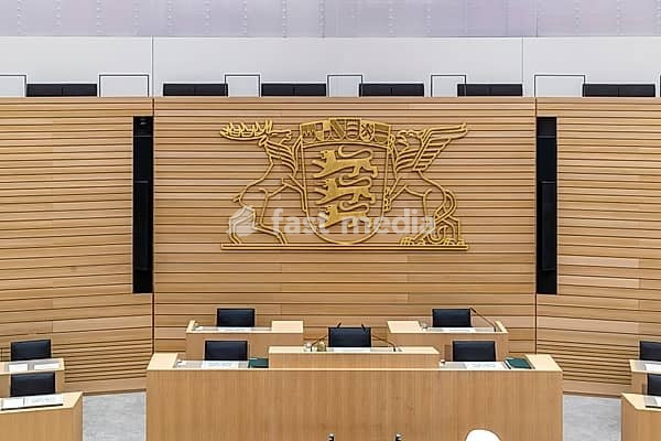 Plenary hall deserted with the seats of deputies and the government bank. Behind it is the coat of arms of the federal state. The state parliament of Baden-Württemberg is the state parliament based in Stuttgart, Baden-Württemberg, Germany