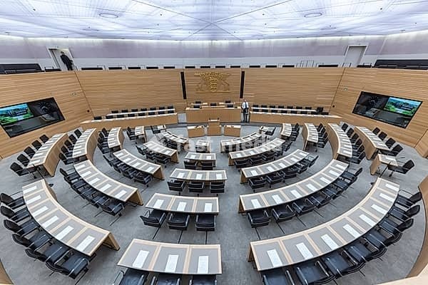 Plenary hall deserted with the seats of deputies and the government bank. Behind it is the coat of arms of the federal state. The state parliament of Baden-Württemberg is the state parliament based in Stuttgart, Baden-Württemberg, Germany