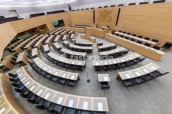 Plenary hall deserted with the seats of deputies and the government bank. Behind it is the coat of arms of the federal state. The state parliament of Baden-Württemberg is the state parliament based in Stuttgart, Baden-Württemberg, Germany