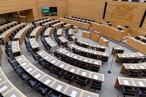 Plenary hall deserted with the seats of deputies and the government bank. Behind it is the coat of arms of the federal state. The state parliament of Baden-Württemberg is the state parliament based in Stuttgart, Baden-Württemberg, Germany