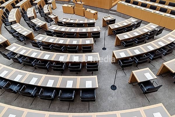 Plenary hall deserted with the seats of deputies and the government bank. Behind it is the coat of arms of the federal state. The state parliament of Baden-Württemberg is the state parliament based in Stuttgart, Baden-Württemberg, Germany