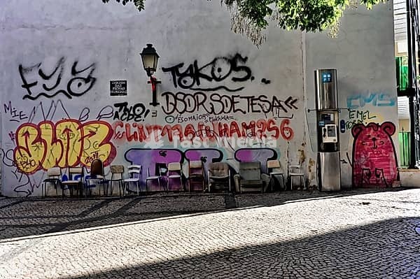 Wall with graffiti, chairs in the shade and a telephone box next to it, Lisbon, Portugal