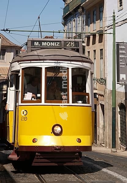 Remodeled Lisbon tram number 28 climbing up a narrow street, with driver and passengers inside, in Lisbon, Portugal
