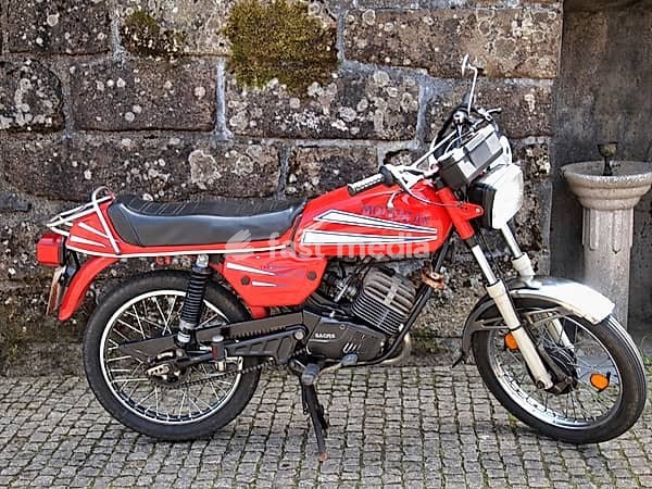 Classic red mobylette motorcycle parked near a stone wall and a stone fountain in Guimarães, Portugal