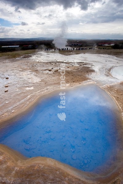 Blue water in geothermal pool with stream from Strokkur Geysir visible in the distance, Geysir, near Reykjavik, Iceland, Polar Regions