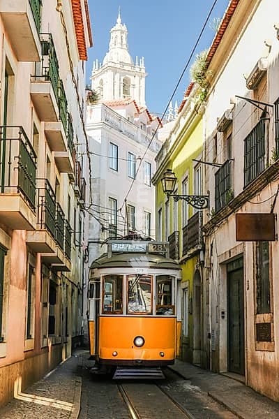Yellow Tram 28 on Narrow Street of Alfama and Monastery of Sao Vicente de Fora on Sunny Day. Lisbon, Portugal