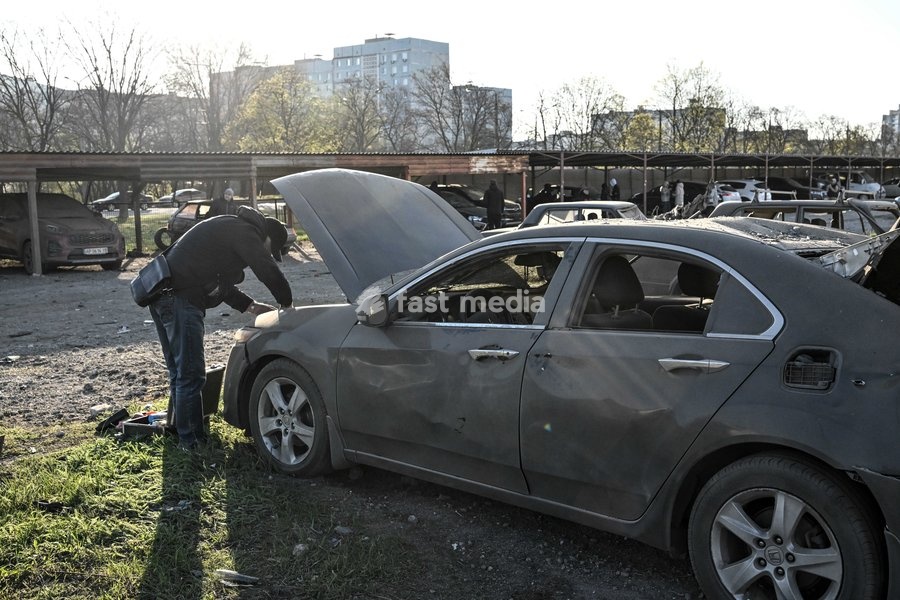 A man examines a car damaged by a Russian drone strike at a parking lot in Zaporizhzhia, Ukraine, April 15, 2026. The attack killed a 74-year-old woman and damaged the stop, a parking lot, and nearby residential buildings