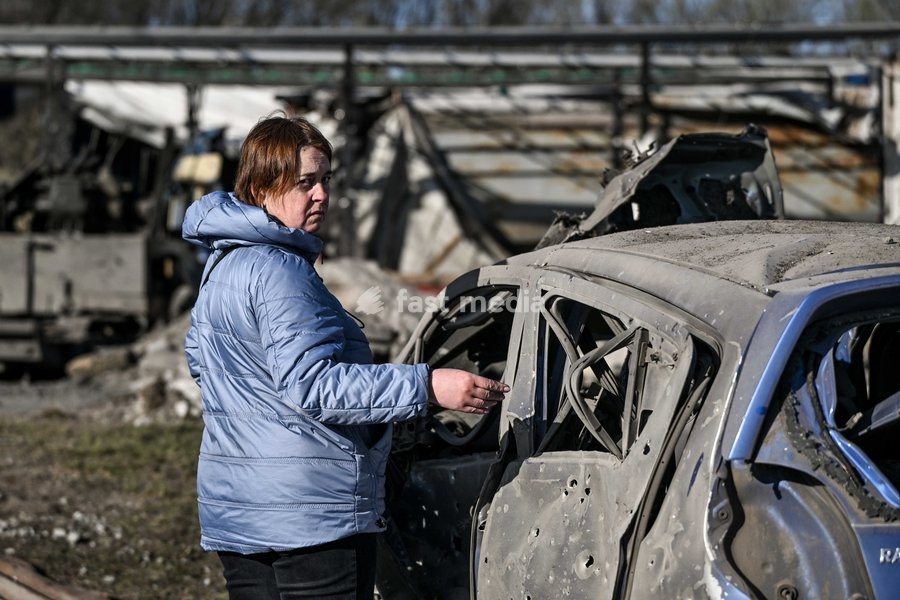 A woman stands by a car destroyed by a Russian drone strike at a parking lot in Zaporizhzhia, Ukraine, April 15, 2026. The attack killed a 74-year-old woman and damaged the stop, a parking lot, and nearby residential buildings