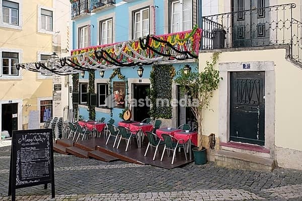 Small restaurant with colorful decorations and outdoor seating area on a cobblestone street in picturesque surroundings, Alfama, Lisbon, Portugal