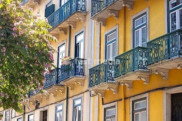Traditional old yellow apartment buildings with wrought iron balconies next to a blooming purple tree in the historic Alfama neighborhood of Lisbon
