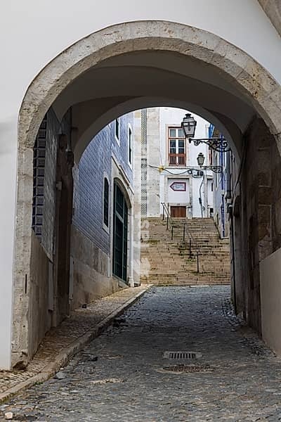 Durchgang durch einen Torbogen in eine kleine Gasse in der Altstadt von Lissabon, Portugal. Archway leading to a narrow alley in the old town of Lisbon, Portugal