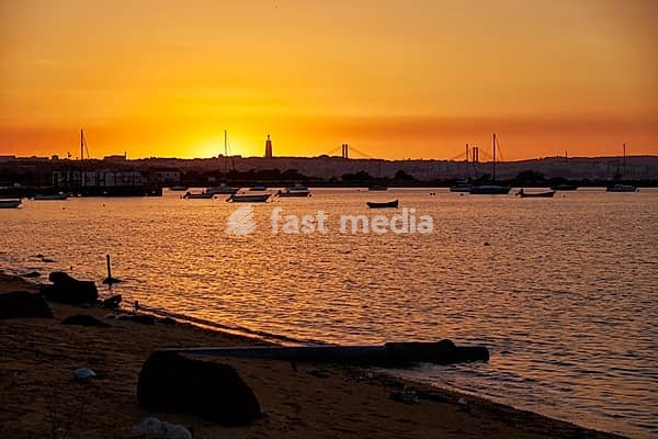 The view of Lisbon city with 25 of April Bridge (Ponte 25 de Abril) and Cristo Rei over the Tagus river from the bank of Seixal in the sunset light. Lisbon. Portugal