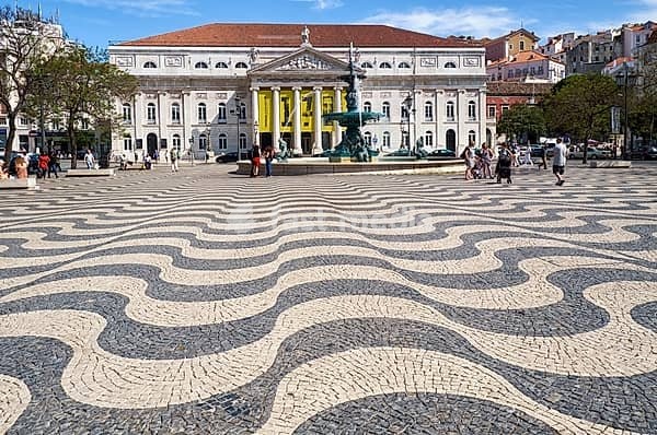 LISBON, PORTUGAL - JUNE 25, 2016: Rossio square with its traditional waves of black and white pavement mosaic, baroque style bronze fountain and National Theatre D. Maria II. Lisbon. Portugal