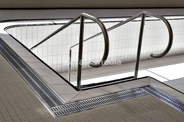 Indoor pool with railing for descending, indoor pool without water with railing to the stairs, white tiles on the indoor pool floor, chrome steel sheet on the edge of the indoor pool, chrome steel railing in the water basin