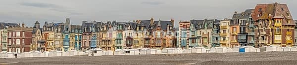 The Belle epoque and Art Nouveau in the seaside resort of Mers-les-Bains. Beach cabins sit on pebbles by the shore. Colorful buildings rise. Mers-les-Bains, Somme, France