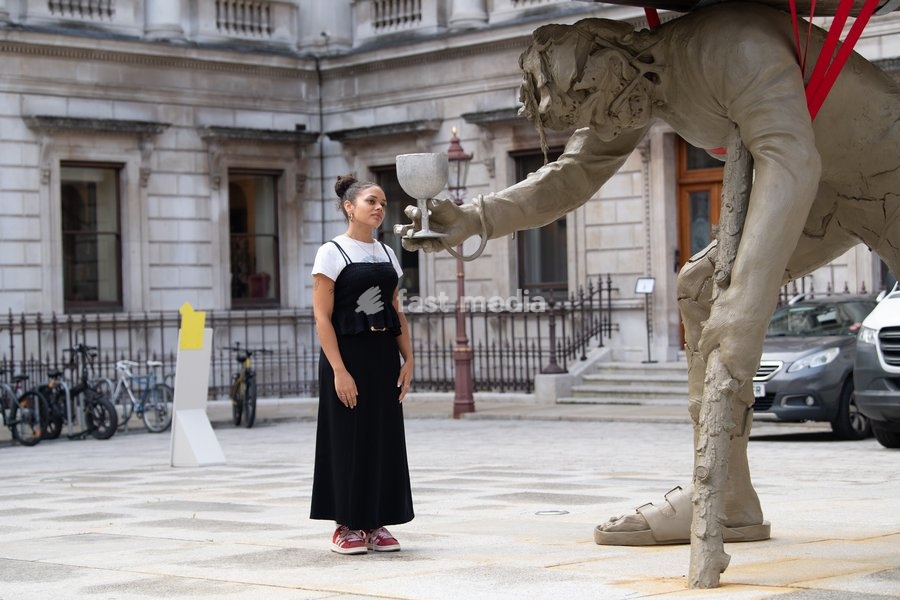 Visitors interact with 'Stack' by Nicole Eisenman, 2022-2024. Made with bronze, oak wood, mineral material, aluminium, and steel and standing at 820 x 335 x 346 cm