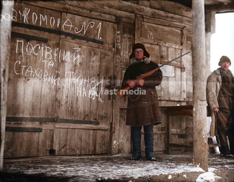 Histoire de l'URSS / Stalinisme / Holodomor Pendant la Grande Famine, un komsomolets (membre des Jeunesses communistes) en faction avec un fusil devant un grenier à blé et à semences de la coopérative agricole « Grigori Petrovski », dans le village de Vilshany, situé aujourd'hui dans le district de…