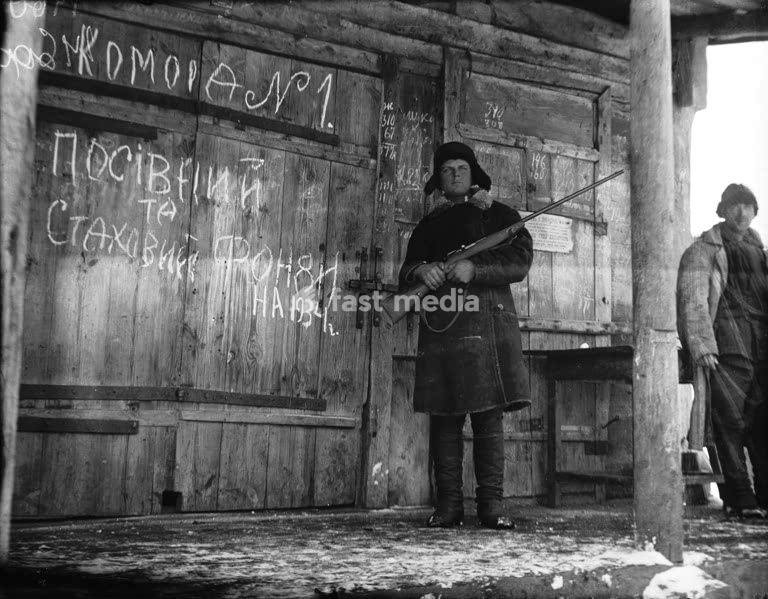 Histoire de l'URSS / Stalinisme / Holodomor Pendant la Grande Famine, un komsomolets (membre des Jeunesses communistes) en faction avec un fusil devant un grenier à blé et à semences de la coopérative agricole « Grigori Petrovski », dans le village de Vilshany, situé aujourd'hui dans le district de…