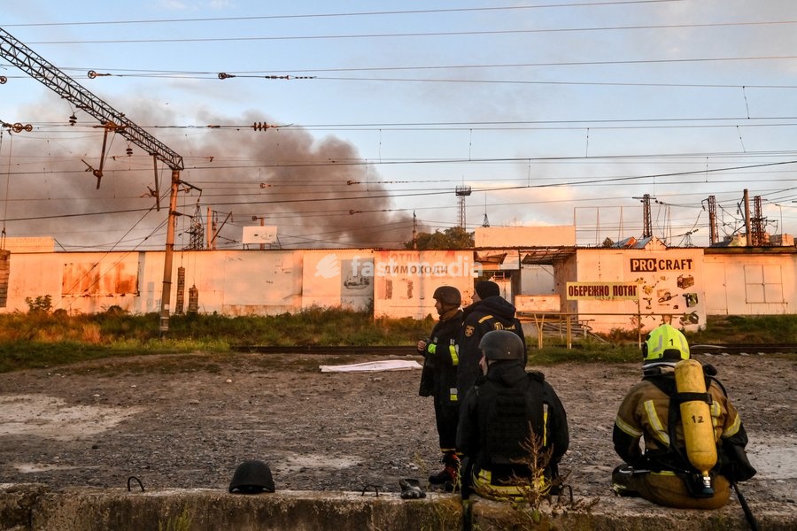 Firefighters stay by the railway tracks as a plume of smoke rises from the Central Clothes Market (Anholenko) in Zaporizhzhia, Ukraine, September 26, 2026. The market sustained significant damage in a Russian drone attack