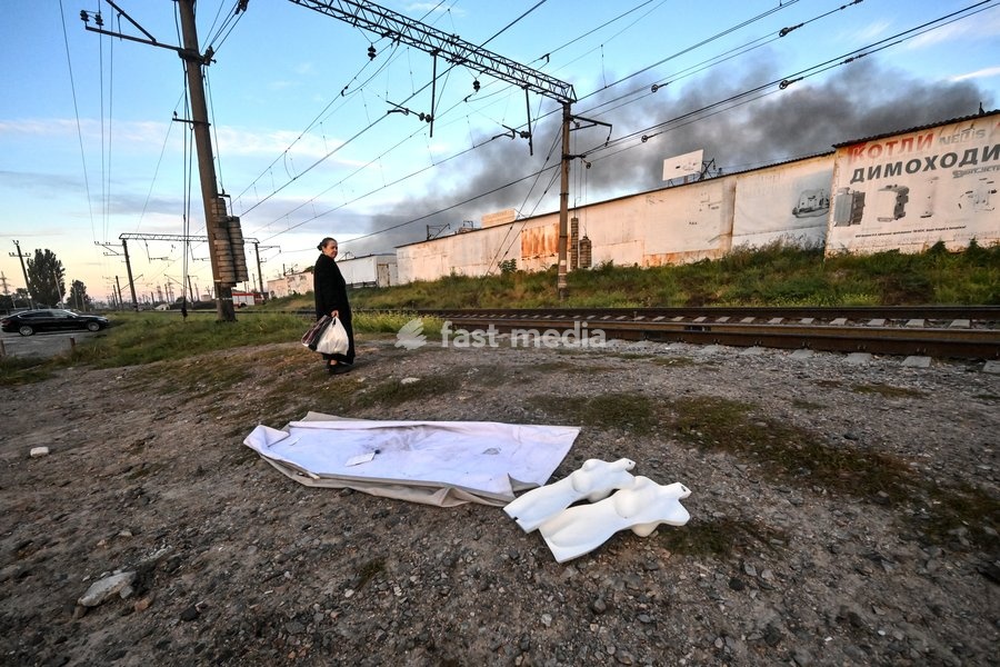 A woman stands at the railway tracks as a plume of smoke rises from the Central Clothes Market (Anholenko) in Zaporizhzhia, Ukraine, September 26, 2026. The market sustained significant damage in a Russian drone attack