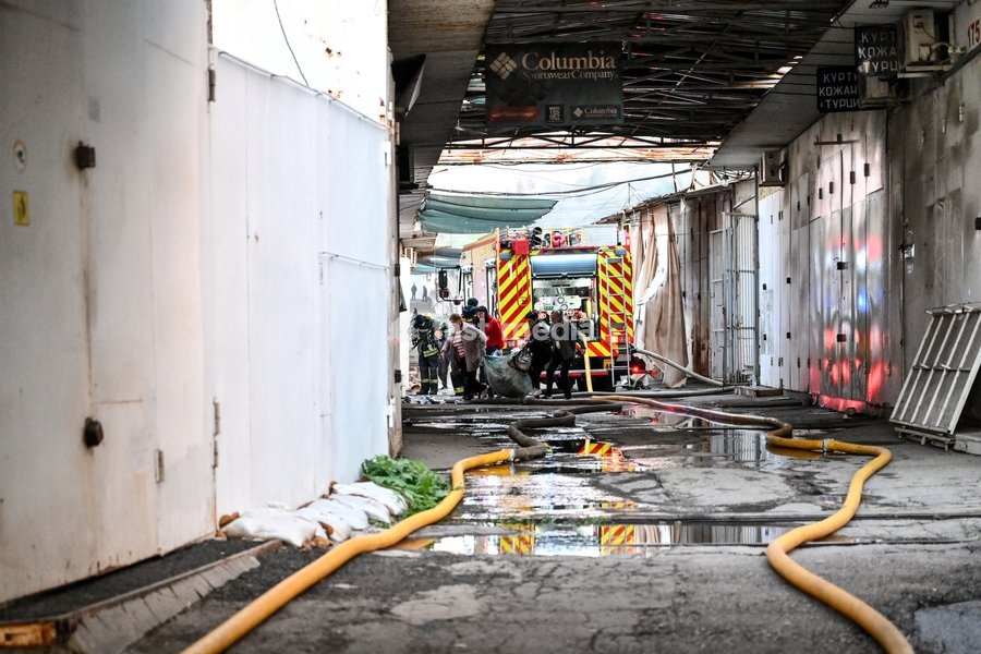 Entrepreneurs carry salvaged goods in a blanket past State Emergency Service rescuers as they roll out fire hoses to extinguish a fire at the Central Clothes Market (Anholenko) in Zaporizhzhia, Ukraine, September 26, 2026. The market sustained significant damage in a Russian drone attack