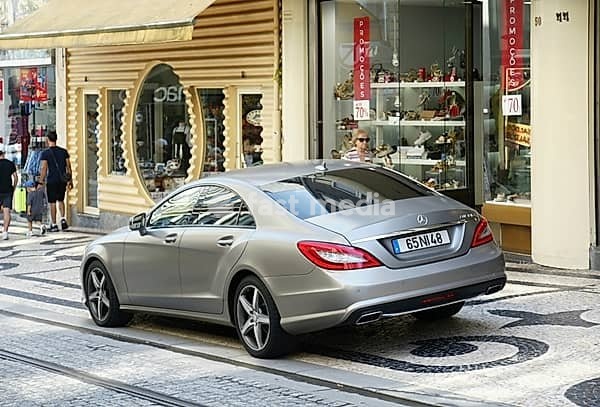 Mercedes-Benz CLS luxury sedan parking on a cobblestone street near shop windows