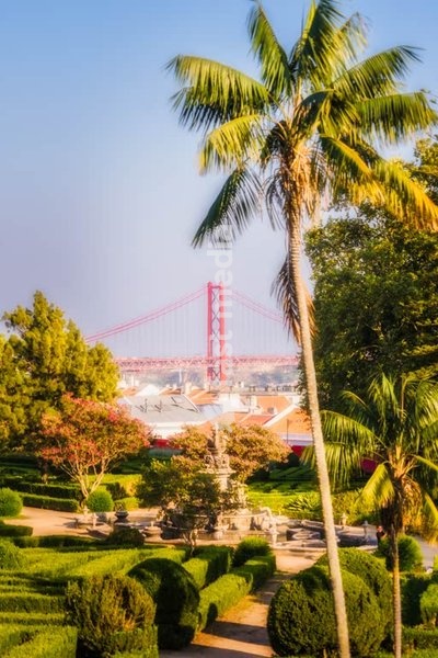 Lisbon, Portugal – Morning light over historic garden Jardim Botánico de Ajuda with fountain and the 25 de Abril Bridge.