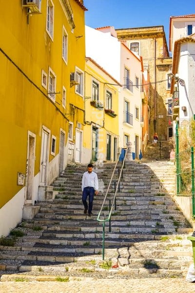 Lisbon, Portugal – man walking down stone steps in the sunny Graça district under blue sky.