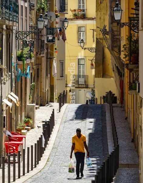 Lisbon, Portugal – A man walking up a narrow cobbled street under warm afternoon sunlight