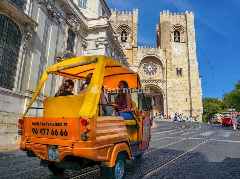 Touristen fahren in einem gelben Tuk-Tuk an einem sonnigem Tag zur historischen Sé-Kathedrale in Lissabon