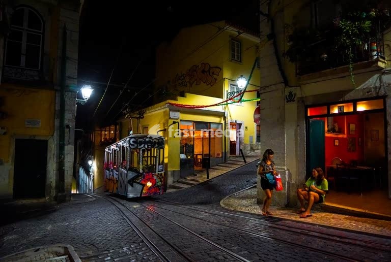 Die Standseilbahn Elevador da Bica fährt nachts die steile Kopfsteinpflastergasse in Lissabon hoch