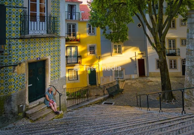 Eine Frau sitzt auf den Stufen vor ihrem Haus im ruhigen Alfama-Viertel in Lissabon, Portugal