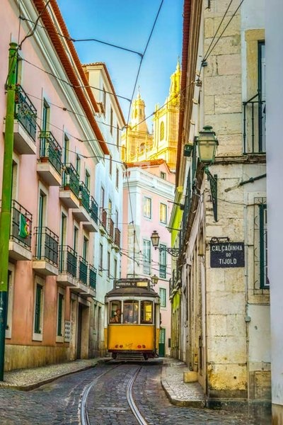 Lissabon, Portugal: Eine gelbe Straßenbahn fährt durch eine schmale Kopfsteinpflastergasse im Stadtteil Alfama zum Konvent São Vicente