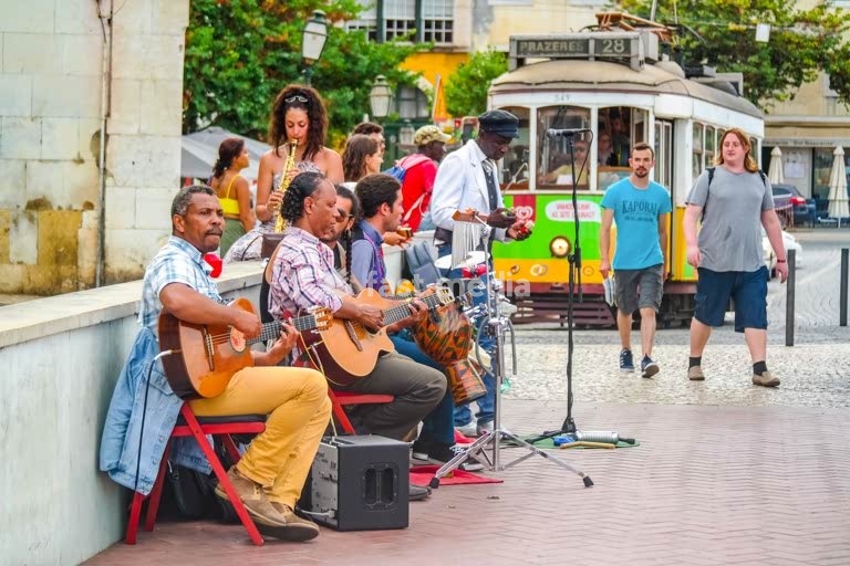 Lissabon, Portugal – Straßenmusiker spielen am Aussichtspunkt Portas do Sol, während hinter ihnen die Straßenbahnlinie 28 vorbeifährt