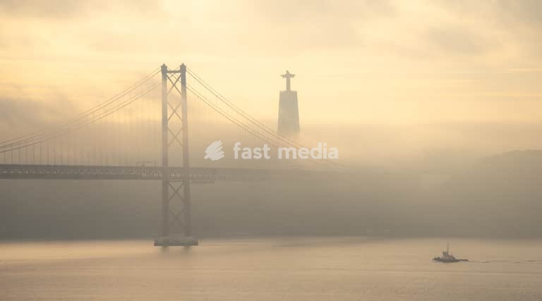 Lissabon, Portugal – Ponte 25 de Abril und Cristo Rei im Morgennebel über dem Tejo. ein Schlepper kehrt zum Hafen zurück