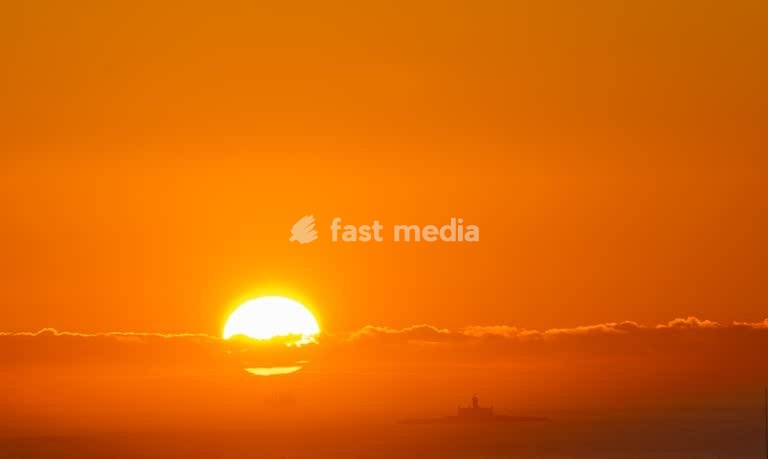 Giant orange sun sets over Farol do Bugio, Lisbon, ship sailing into golden hour
