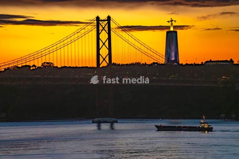 Ponte 25 de Abril bridge silhouetted at sunset with Cristo Rei statue, Lisbon, Portugal