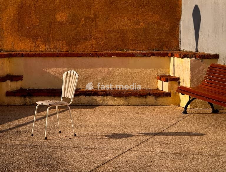 Empty chair and bench cast long shadows on quiet terrace at dawn, Lisbon, Portugal