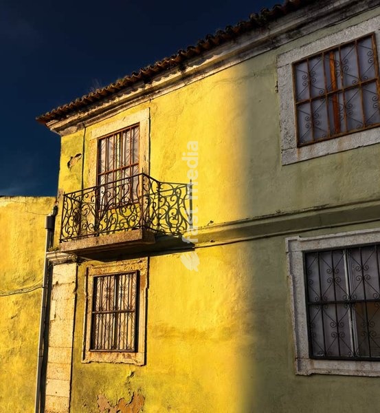 Weathered yellow facade with wrought iron balcony split by shadow, Portugal, mood shot