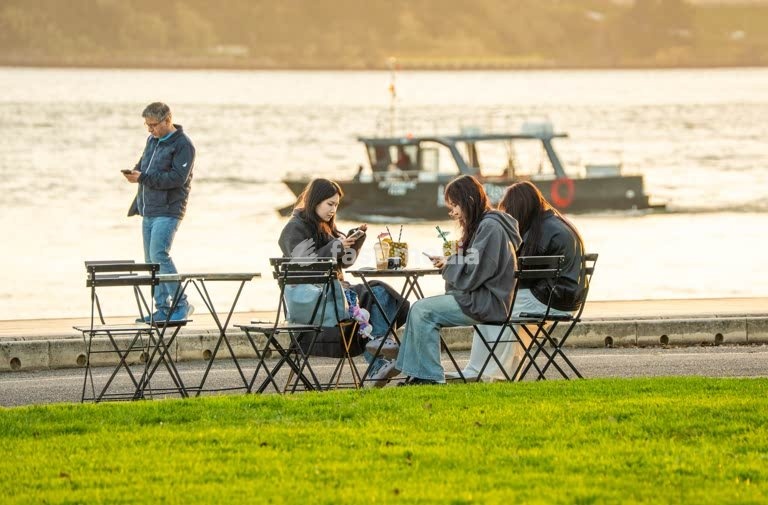 Tourists absorbed in smartphones, boat and sunset passing unnoticed, Tagus riverside, Lisbon