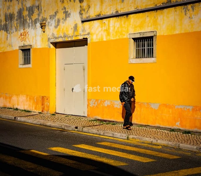 Moody street photography, solitary man by yellow wall and zebra crossing, Alcântara, Lisbon, Portugal. Photo Peter Delius