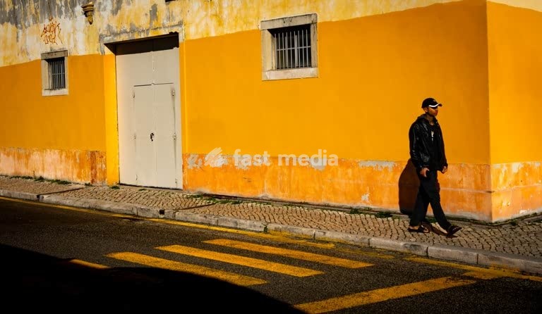 Moody street photography, solitary man by yellow wall and zebra crossing, Alcântara, Lisbon, Portugal
