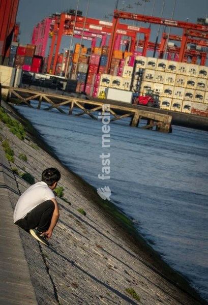 A thoughtful young man on Tagus embankment, container port cranes, Alcântara, Lisbon, Portugal