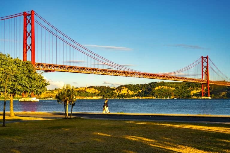 A couple walking near bridge Ponte 25 de Abril across Tagus river in Lisbon, Portugal