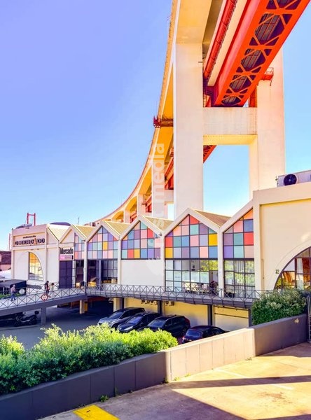 Colorful architecture of Mercado de Alcântara under dramatic 25 de Abril Bridge structure, Alcântara, Lisbon, Portugal