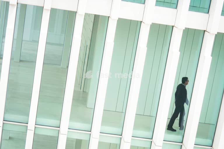 Lone businessman walking through minimalist glass and white column interior, modern architecture