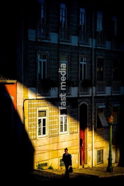 Cinematic chiaroscuro: lone figure caught in dramatic shaft of light, Lisbon, Portugal