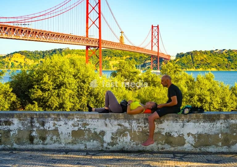 Couple resting by Ponte 25 de Abril and Cristo Rei, Tagus River, Lisbon, Portugal
