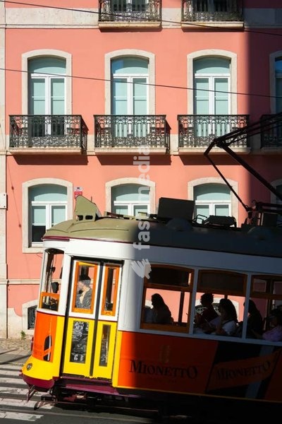 Classic yellow tram passing pink facade with balconies, Alcântara, Lisbon, Portugal