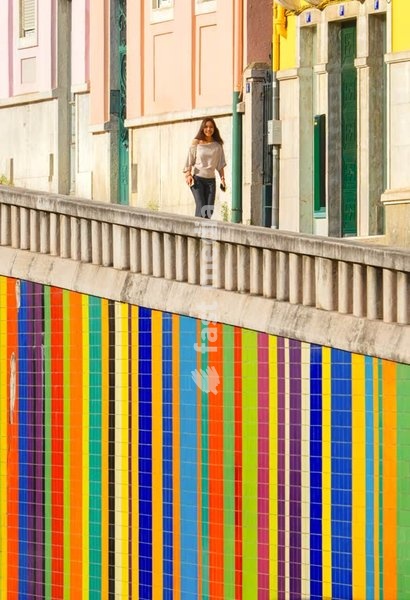 Colorful tiled wall contrasts traditional house facades, woman walking, Av. Infante Santo, Lisbon, Portugal – urban street photography